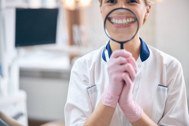 Χαρούμενη γυναίκα οδοντίατρος με μεγεθυντικό φακό στα χέρια - Φωτογραφία, εικόνα