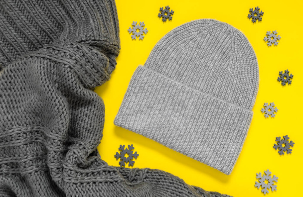 Sweter lub szalik i kapelusz z dzianiny w modnych kolorach roku 2021, oświetlający żółty i ostateczny szary. Modne ciepłe zimowe ubrania i akcesoria. Tekstura wełny i szare płatki śniegu - Zdjęcie, obraz