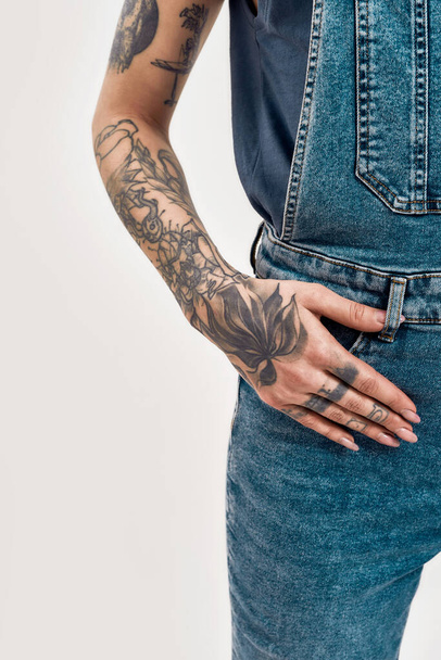 A tattooed hand lying over a denim overall of a white woman - Photo, image