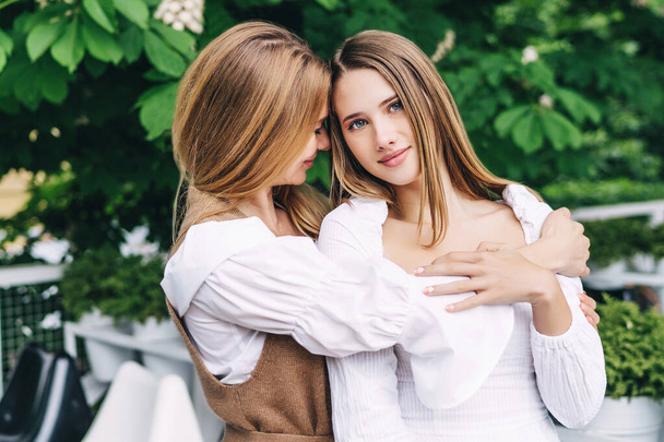 Photo of two sisters holding hands and smiling at the camera, one of them holding flowers in her hands - Фото, зображення