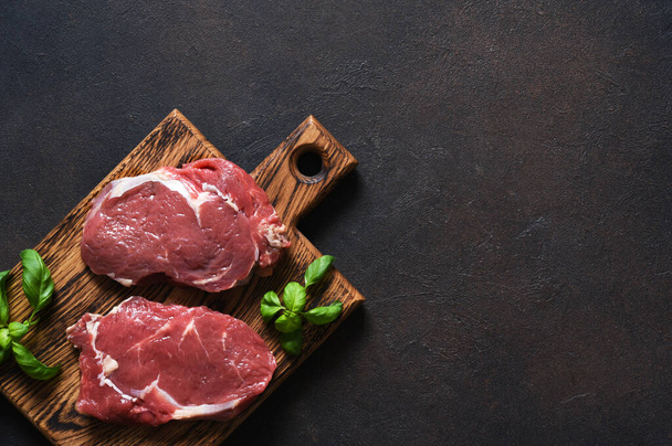 Raw cooking Ribeye beef steak with basil on a wooden board. View from above - 写真・画像
