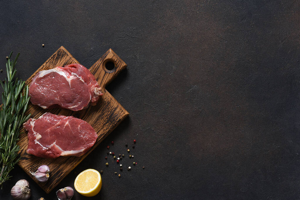 Raw Ribeye beef steak cooking with ingredients: salt, pepper, lemon. Top view with copy space - 写真・画像