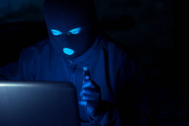 Delito cibernético, piratería y crimen tecnológico. hacker enmascarado que trabaja en la oscuridad robando datos e información de identidad personal de una computadora portátil. - Foto, imagen