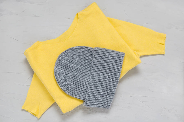 Bonnet et pull gris tricoté aux couleurs tendance de l'année 2021 illuminant le jaune et le gris ultime. Vêtements et accessoires d'automne et d'hiver chauds à la mode. Texture de laine sur fond de béton - Photo, image