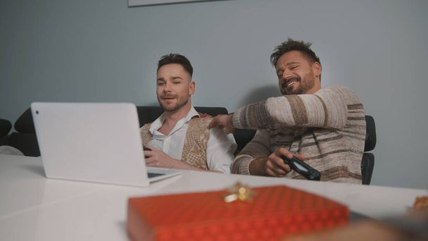 Glückliches homosexuelles Paar oder beste Freunde, die Videospiele spielen. Geschenk im Vordergrund - Foto, Bild