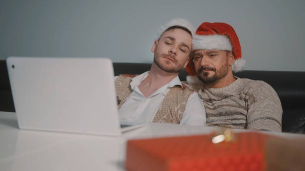 szczęśliwy gej mężczyzna para z Santa Claus kapelusze przytulanie i oglądanie film na w Wigilia - Zdjęcie, obraz