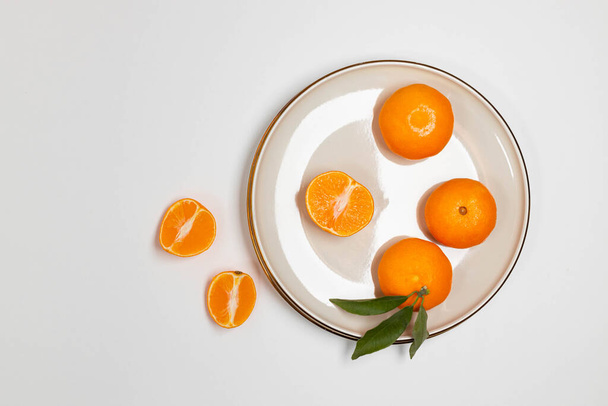 Frutas frescas de mandarina o clementina en un plato beige con un borde de oro sobre la mesa. Fondo de fruta de colores. Piso tendido, vista superior, espacio para copiar. Composición decorativa navideña - Foto, Imagen