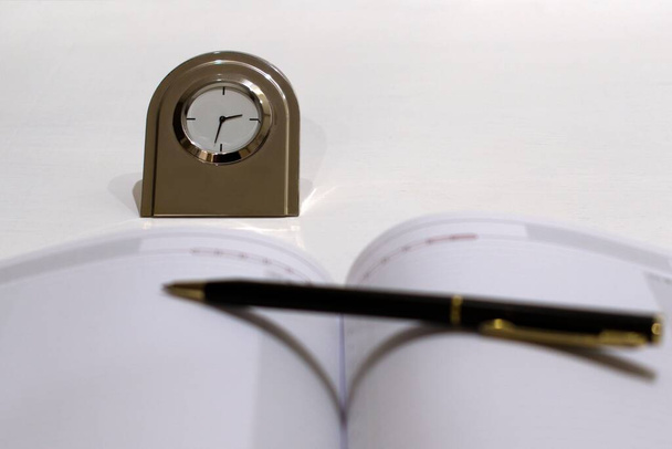Günlük ve tükenmez kalemle bulanık önplanı olan metal masa saati. - Fotoğraf, Görsel