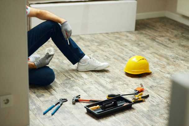 Home repairs. Cropped shot of handyman holding screwdriver and wall plug socket. Home repair hand tools on laminate flooring. Home improvement - 写真・画像