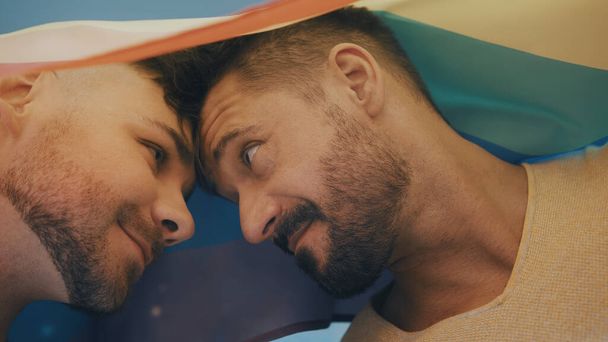 Portret dwóch młodych przystojnych homoseksualistów pokrytych tęczową flagą patrzących na siebie - Zdjęcie, obraz
