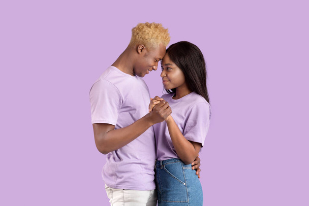 Couple noir romantique tenant leurs mains, touchant le front, étant intime et affectueux sur fond violet - Photo, image