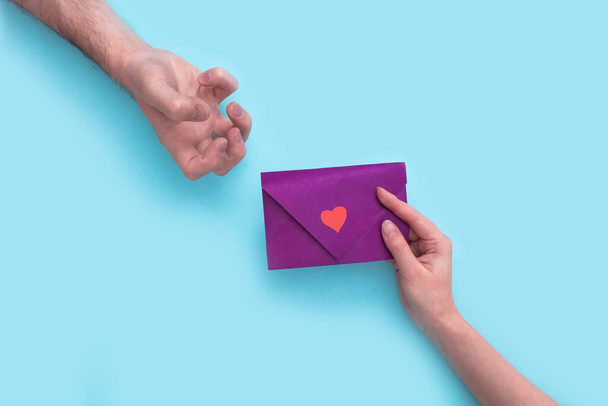 Naisen käsi pitää violettia kirjekuorta ystävänpäivänä ja antaa sen miehelle, joka ilmaisee negatiivisia tunteita kehon kielellä. inhoavat. - Valokuva, kuva