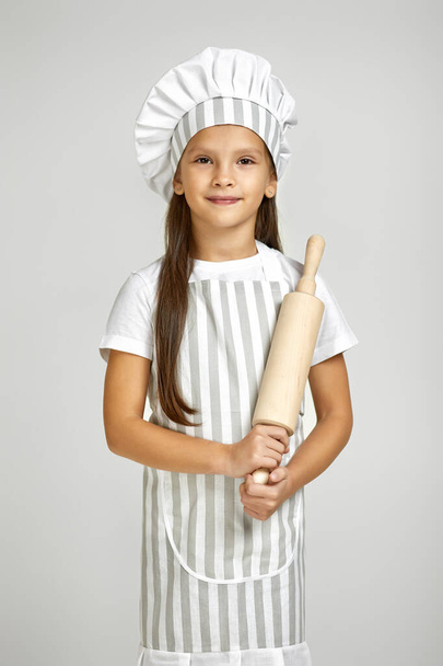 cute little girl in chef hat and apron holding rolling pin - Foto, afbeelding