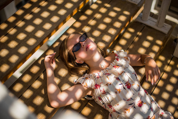 Güneşli bir yaz gününde plajdaki kafede güneş gözlüğü takan güzel bir kızın moda portresi. Genç, zayıf, güzel kadın yaz tatili, güneşli.. - Fotoğraf, Görsel