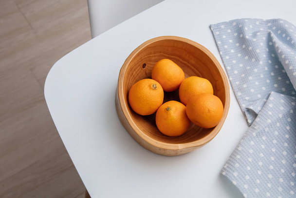 Top view of fresh mandarin oranges or tangerines in the wooden bowl on the white table in the kitchen - Foto, immagini