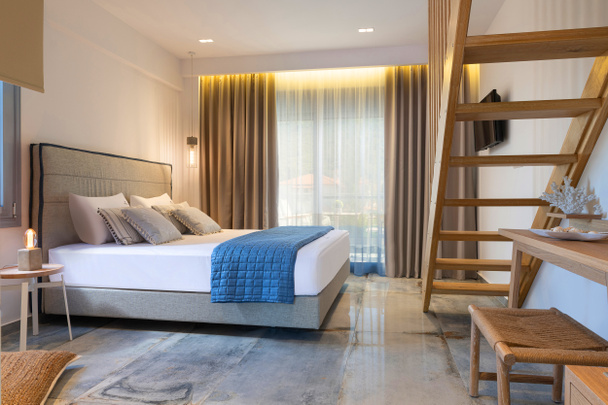 Современный интерьер в морском стиле: белая спальня с деревянной лестницей, мебель ручной работы, серая мягкая текстильная двуспальная кровать - Фото, изображение