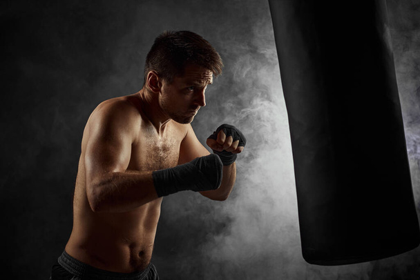 Male boxer punching in boxing bag on black background - Foto, imagen