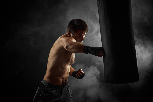 boxer in black boxing wraps punching in boxing bag - Foto, afbeelding