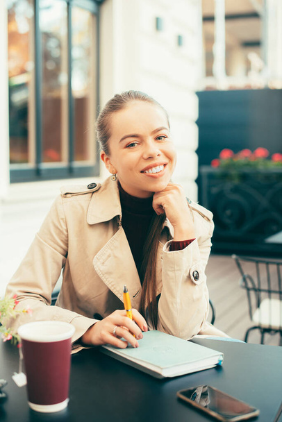 Πορτρέτο της χαρούμενης νεαρής γυναίκας που κάθεται στο καφέ και έχοντας χρόνο για ένα φλιτζάνι τσάι - Φωτογραφία, εικόνα