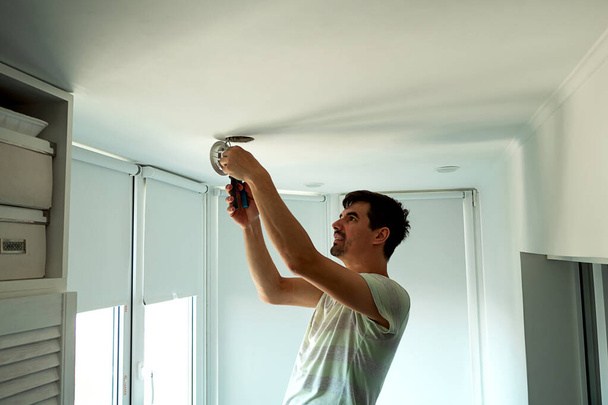 House master male electrician repairs ceiling light indoor home in white room - Fotografie, Obrázek