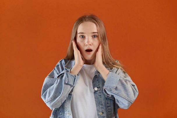 A frightened girl looks at the camera with her mouth open. Orange background. - Foto, afbeelding