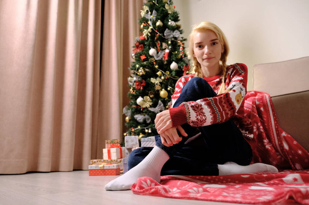 Beautiful young blonde woman sitting on a blanket near the Christmas tree. - Фото, зображення