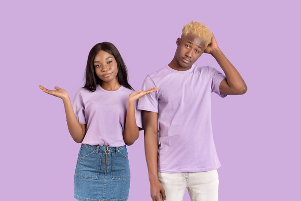 Wer weiß. Porträt eines jungen schwarzen Paares achselzuckend auf violettem Studiohintergrund - Foto, Bild
