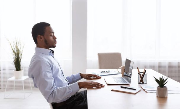Schwarzer Geschäftsmann sitzt mit geschlossenen Augen vor Laptop - Foto, Bild