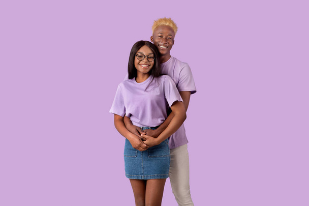 Cooles schwarzes Millennial-Paar umarmt sich vor violettem Studiohintergrund - Foto, Bild