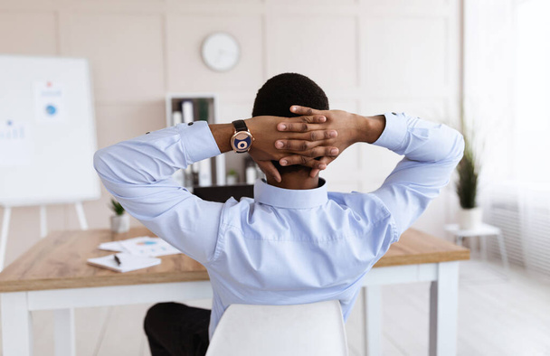 Rückenansicht eines schwarzen Geschäftsmannes, der im Büro am Arbeitsplatz sitzt - Foto, Bild
