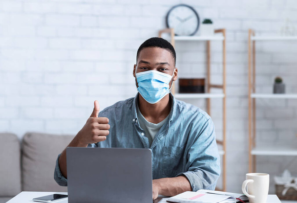 African Man Wearing Mask Sitting At Laptop Gesturing Thumbs-Up Indoor - Photo, Image
