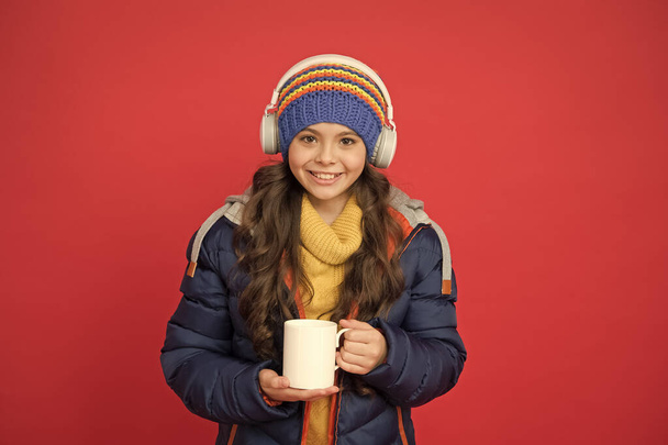 Warming up. Hipster fashion trend. Happy winter holidays activity. Feeling warm and happy. Comfy style. Cheerful smiling child in stylish outfit. Winter wardrobe. Listening music and drinking cocoa - Photo, image