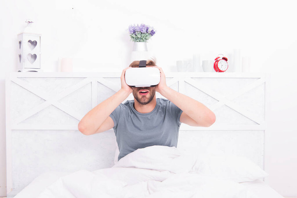 Virtual reality is truly here. Caucasian man wearing virtual reality headset in bedroom. Handsome guy using virtual reality device in bed. The next generation of virtual reality - Photo, Image