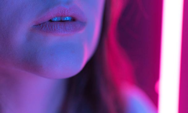 Colorful lips of a young woman in the light of neon close-up. Beauty and fashion in a nightclub - Фото, изображение