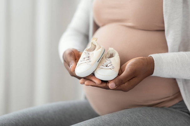 Naissance en attente. Femme enceinte noire assise avec de petites chaussures de bébé dans les mains - Photo, image