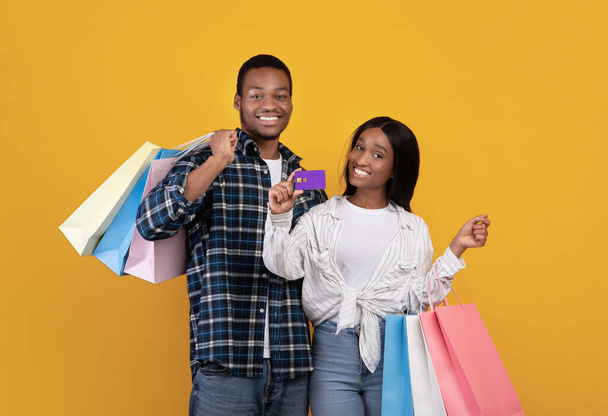 Uśmiechnięta młoda afrykańska para studentów z wieloma kolorowymi torbami na zakupy pokaż kartę kredytową - Zdjęcie, obraz