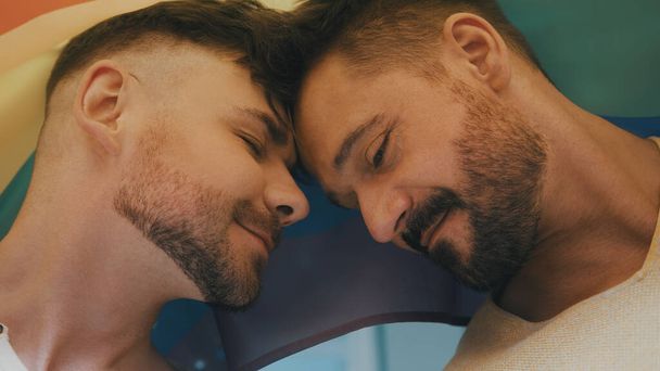 Porträt zweier junger, gut aussehender homosexueller Männer mit Regenbogenfahne, die einander anschauen - Foto, Bild