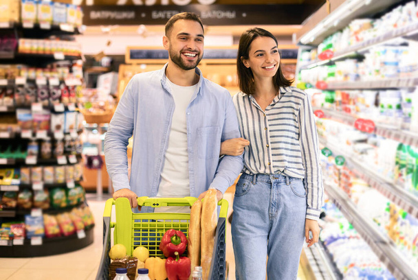 Young cheerful couple with the cart shopping in supermarket - Photo, Image