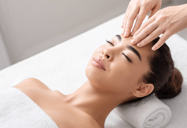 Masaje antiarrugas. Joven mujer asiática relajante durante el tratamiento de belleza en el salón de spa - Foto, imagen
