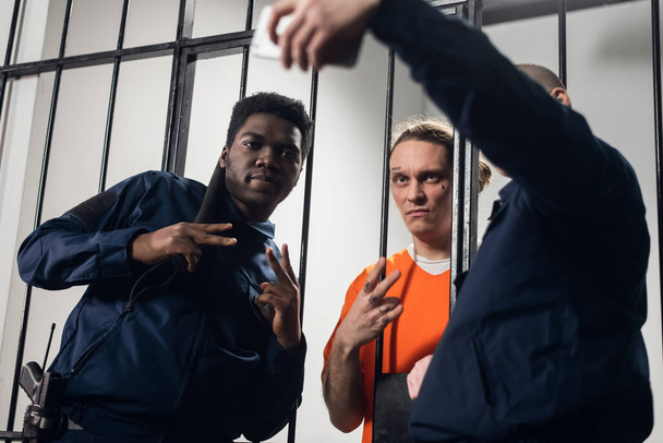 Actores en el set de una película sobre la prisión hacen un selfie divertido en una celda de la prisión en el fondo de las barras. - Foto, Imagen