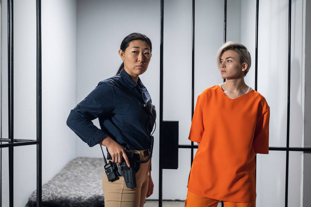 Dreharbeiten für einen Film über ein Frauengefängnis. Backstage. Asiatische Aufseherin und ein kriminelles Mädchen in einem gelben Gewand auf dem Hintergrund einer Gefängniszelle. - Foto, Bild