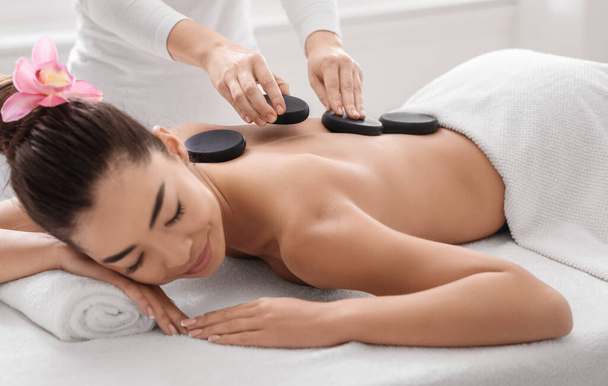 Beautiful asian woman getting massage with hot stones at modern spa salon - Photo, Image