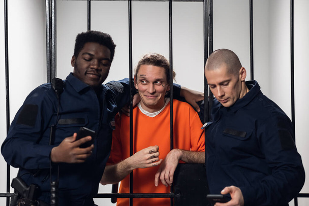 Yüzünde dövmesi olan bir mahkum, gardiyan arkadaşlarıyla birlikte akıllı telefondan selfie çekiyor.. - Fotoğraf, Görsel