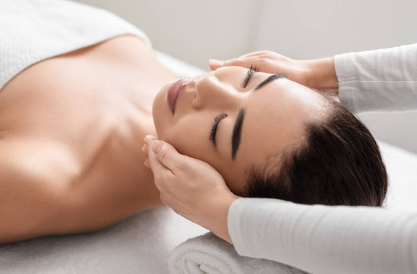 Jeune femme asiatique relaxant pendant la séance de massage du visage au salon de beauté spa - Photo, image
