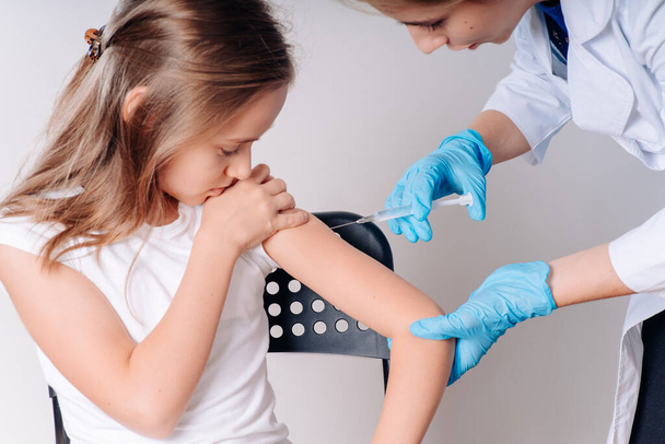 Het meisje wordt gevaccineerd door een arts in een witte jas. Vaccinatie. Bestrijding van ziekten.COVID 19. Het concept van de gezondheidszorg tijdens een epidemie - Foto, afbeelding