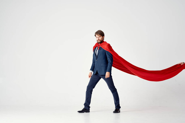 uomo d'affari in un mantello rosso su uno sfondo chiaro guarda alla tuta supereroe successo laterale - Foto, immagini
