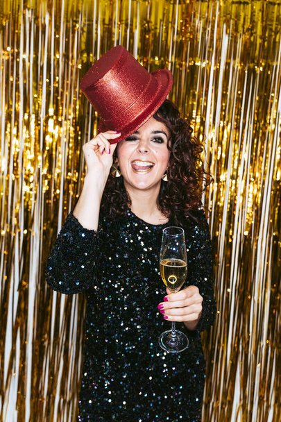パーティの衣装に身を包んだ美しい女性がシャンパンのグラスを持ち、カメラでクリスマスのトップハットと挨拶をしながら大晦日を祝います。新年会のコンセプト - 写真・画像
