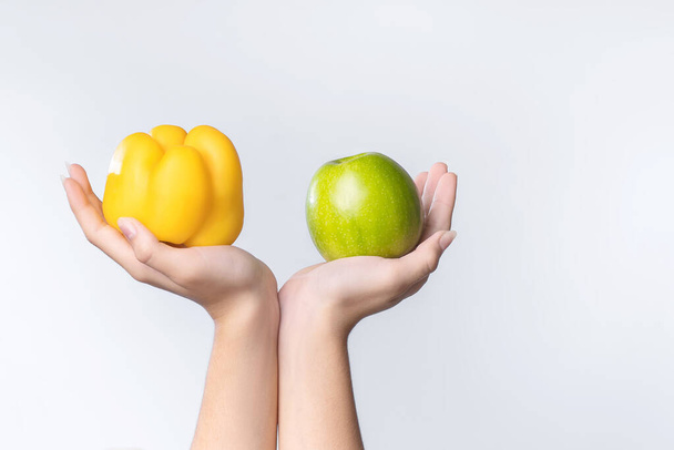 Σούπερ φαγητό σε λευκό φόντοΧέρια ενός κοριτσιού με ένα λαχανικό και ένα φρούτο.Κίτρινο πιπέρι και ένα πράσινο μήλο στις παλάμες ενός κοριτσιού. Υγιεινή τροφή. - Φωτογραφία, εικόνα