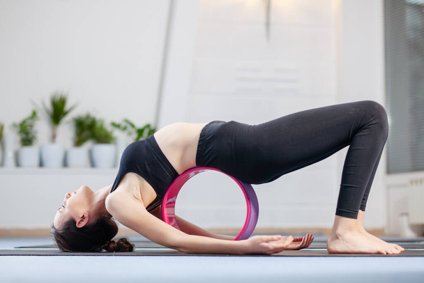 Yoga girl exercising on yoga wheel in a studio. - 写真・画像