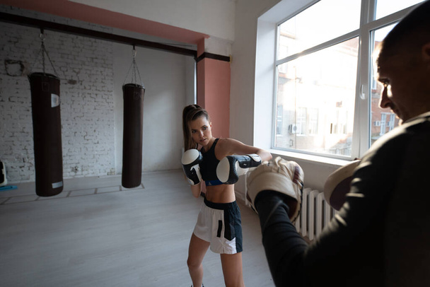 Mladá dívka diriguje trénink kickboxu a cvičí údery tlapkou s profesionálním boxerem - Fotografie, Obrázek
